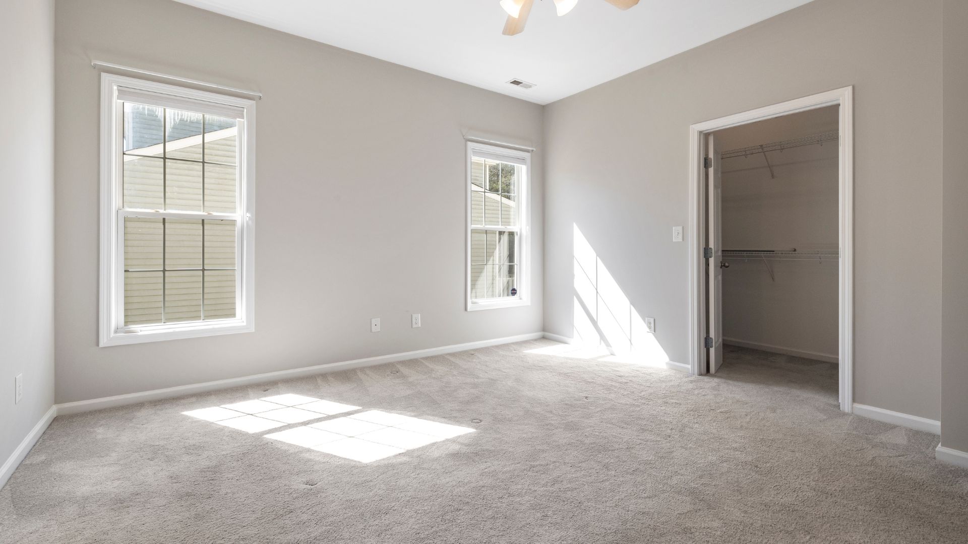 Empty bedroom with carpet, windows, and walk-in closet, bathed in natural light