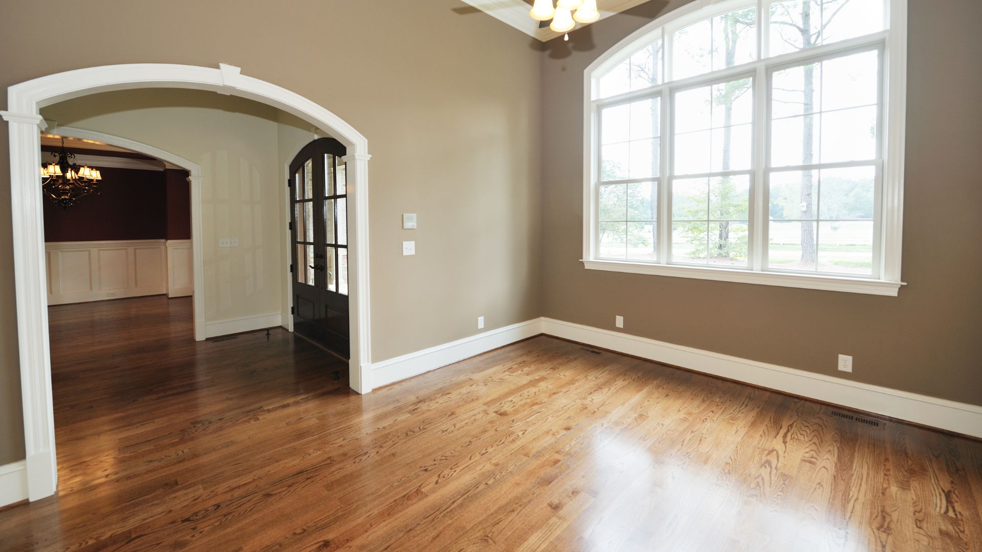 Empty room with hardwood floors, white trim, arched doorway, and large windows